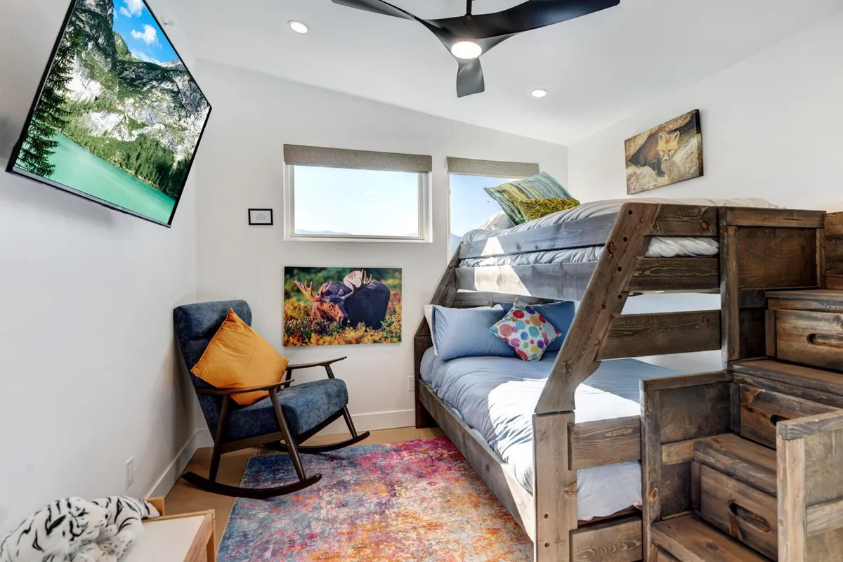 A cheerful bunk bedroom featuring a bunk bed, colorful pillows, a rocking chair, wall art, and a TV. The layout is playful yet comfortable, offering options for families and providing in-room entertainment.