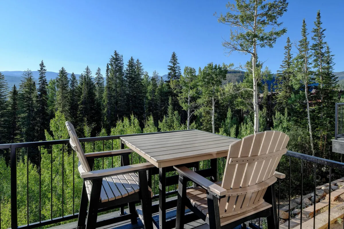 An outdoor seating area nestled among tall trees provides a peaceful place to relax, with a clear view of distant mountains. The arrangement suggests opportunities for wildlife observation, sunrise or sunset watching, and tranquil moments after a day of exploring.