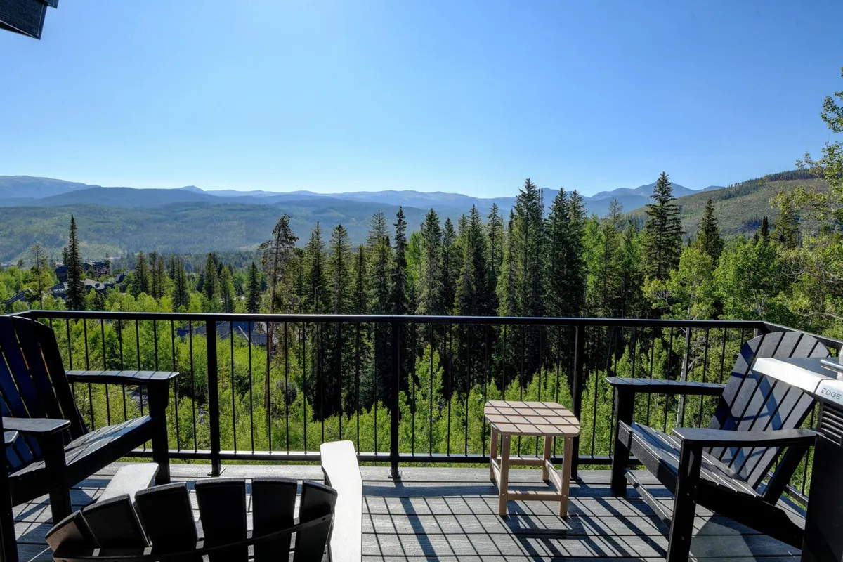 An inviting exterior view from the chalet’s balcony, overlooking a tranquil stretch of forest and sweeping mountain views. The balcony seating suggests a perfect spot to unwind and enjoy the surrounding natural beauty after a day of adventure.