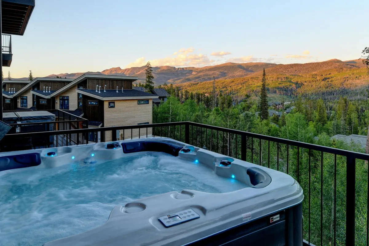 An inviting outdoor hot tub sits on a balcony overlooking stunning mountain views. The warm water, surrounded by wooden chalets and natural beauty, hints at relaxation after a busy day of activities. The atmosphere is tranquil and luxurious, ideal for unwinding as a group.