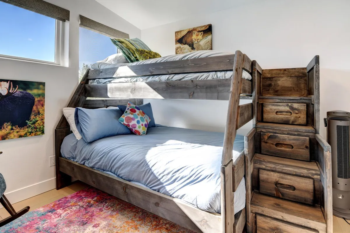 A playful and inviting bunk bedroom with a twin-over-full bunk bed, colorful throw pillows, and a staircase with built-in storage. The room exudes a cheerful vibe, ideal for children or families, with ample space for games and reading.