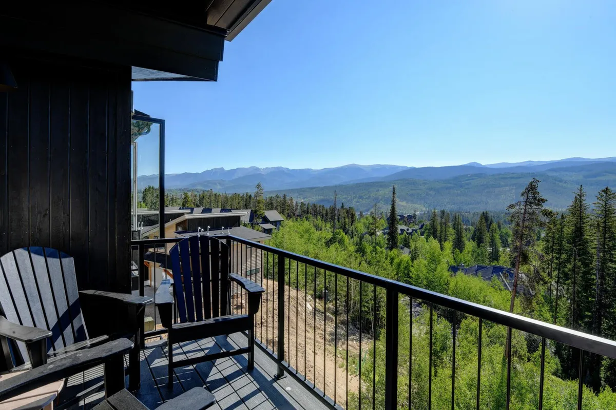 An exterior deck view looking out to the surrounding mountains and trees, with deck chairs poised for relaxation. The image highlights the immediate outdoor environment and the chalet's connection to the natural landscape, creating a peaceful first impression for visitors.