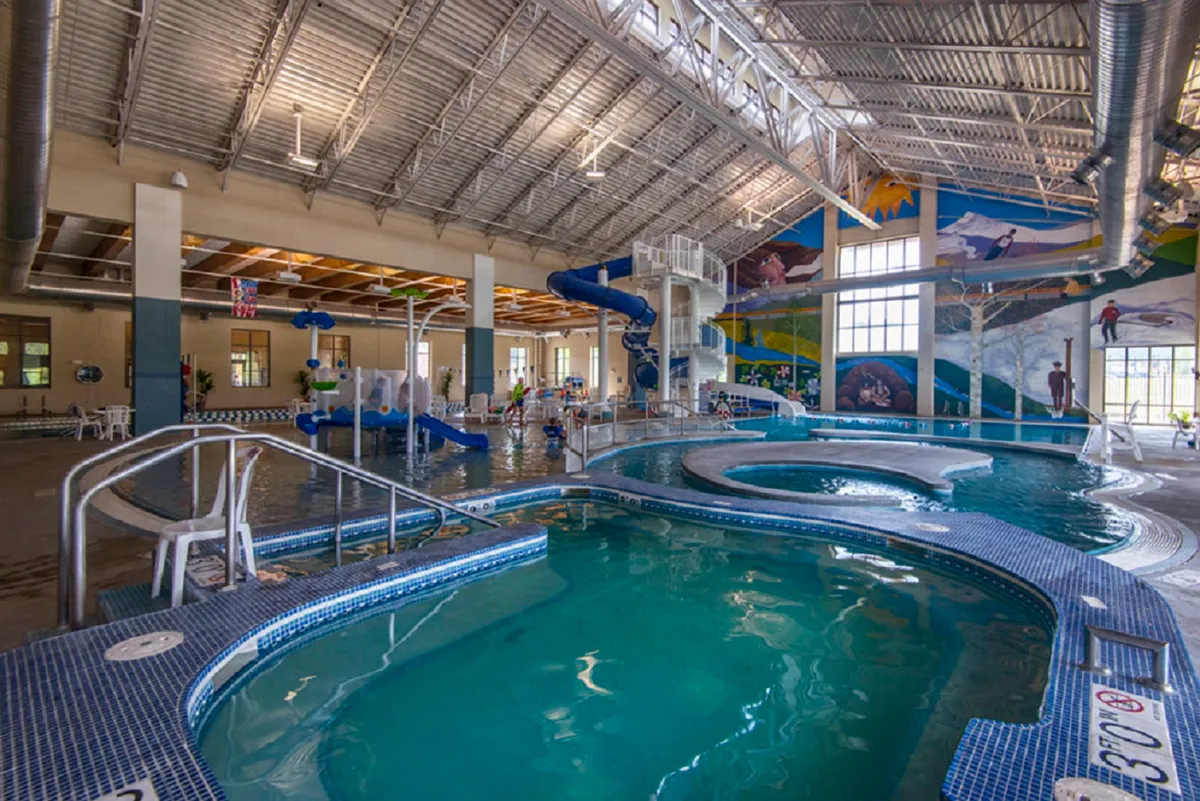 This image captures a lively indoor swimming facility, featuring children playing on water slides and enjoying the swimming pool. The space is colorful and energetic, with a mural on the wall adding visual interest. The joyful activities of kids highlight family-friendly recreation options.