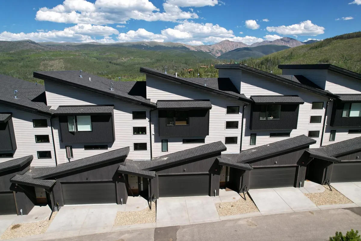 A sleek, contemporary exterior showing modern rooftops set against a stunning mountain backdrop. The setting is serene yet close to nature, suggesting proximity to both the outdoors and the amenities of town.