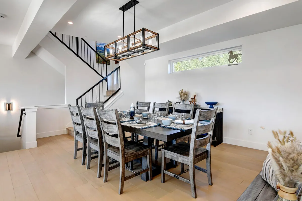 A sophisticated dining area with a large table sits beneath a stylish chandelier; the space is adjacent to a staircase and designed for group meals, family gatherings, and celebrations. The warm atmosphere and layout encourage togetherness and memorable shared experiences.