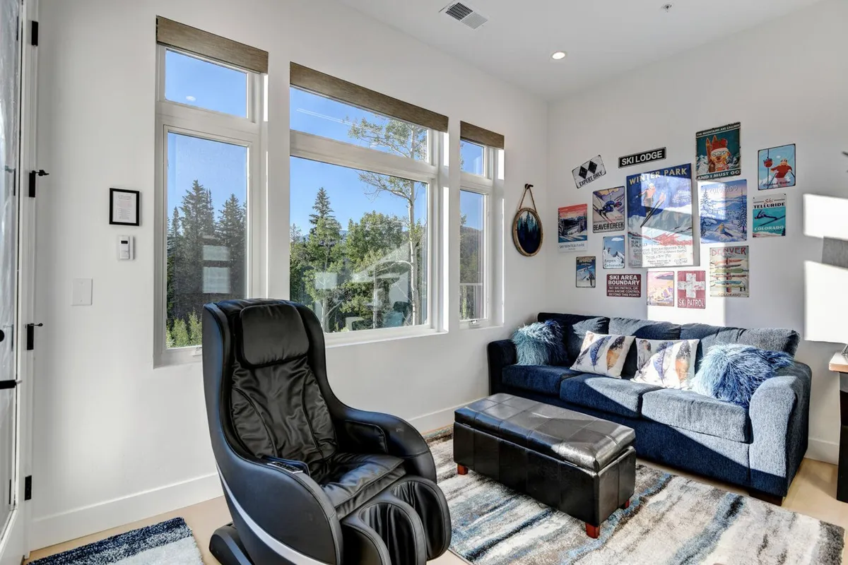 A spacious, comfortable living area with large windows, a cozy sofa, a comfortable chair, and cheerful wall art. The room is bright and welcoming, set up as an ideal spot for board games, movies, or relaxed family gatherings.