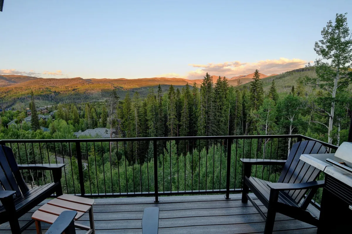 This exterior image features the chalet nestled in a lush forest, with a clear view of the mountains and outdoor seating visible. The scene exudes a tranquil and inviting atmosphere, situating the chalet in its natural context and hinting at the property's immediate surroundings.